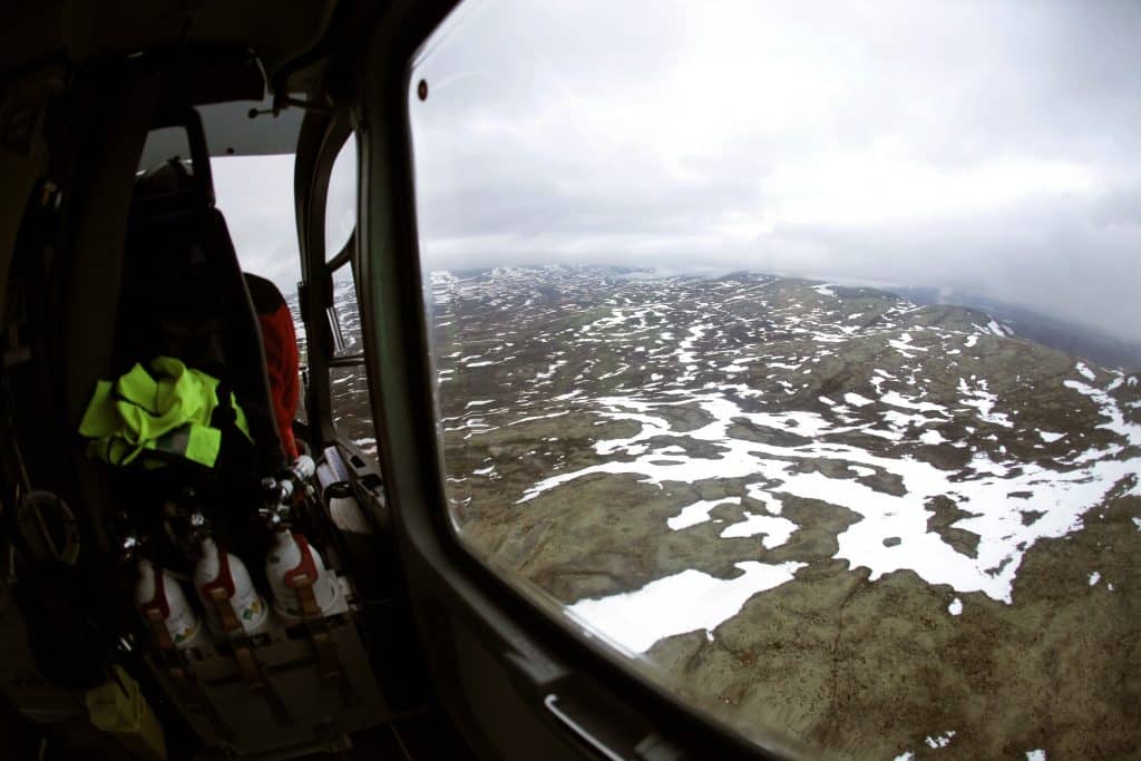 Utsikt over snødekte fjell sett gjennom helikoptervindu. 