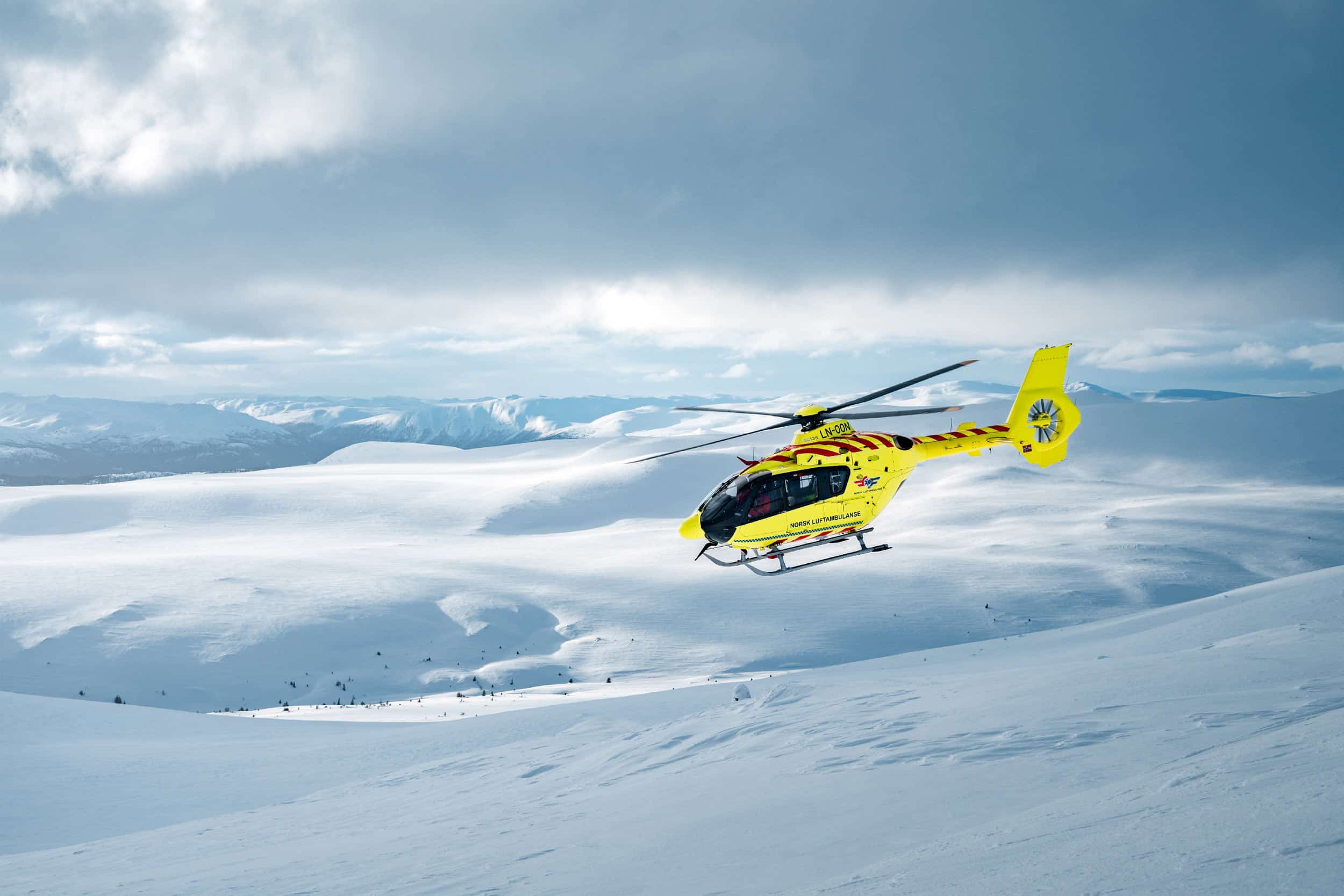 Luftambulansehelikopter flyr over snødekt landskap