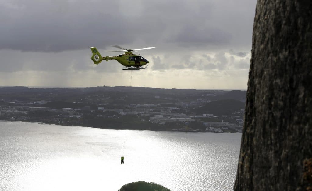 Helikopter som flyr over vann med redningsmann hengende under. 